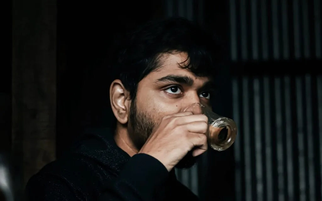 A young man sitting alone with a cup of tea, looking thoughtful